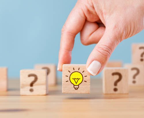 Woman hand picked wooden cube block with light bulb icon and question mark symbol